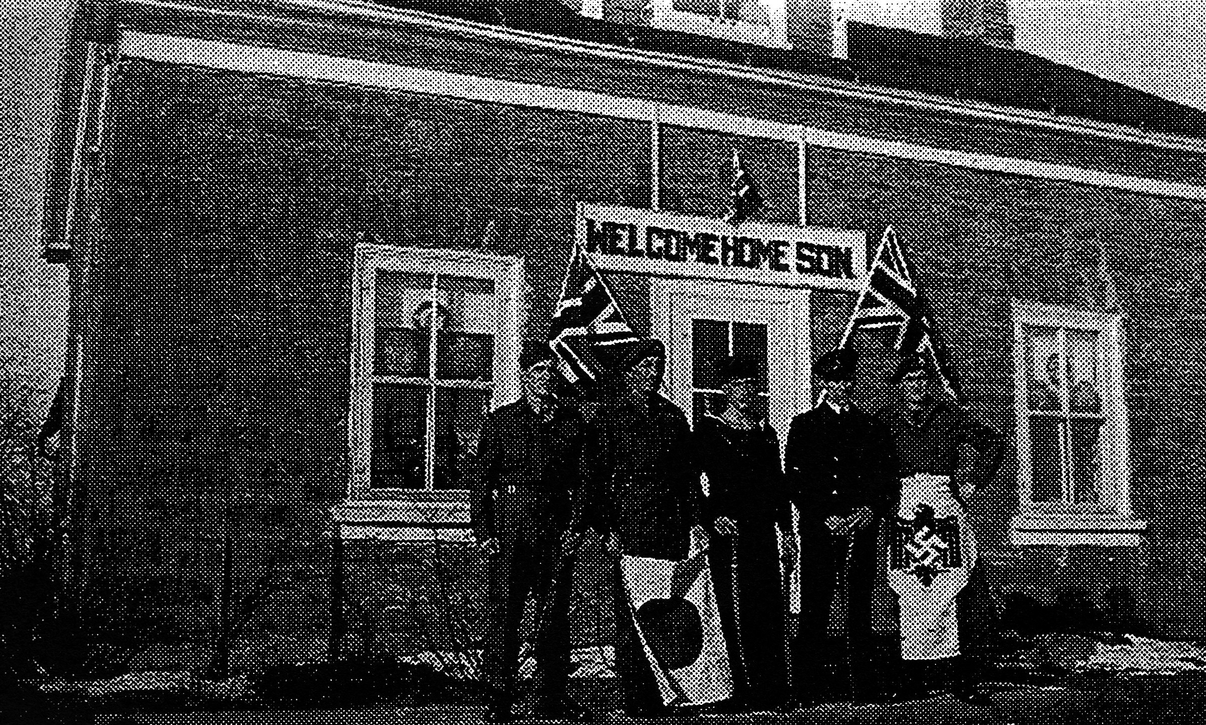 house with a large welcome sign above the door and five persons standing in front